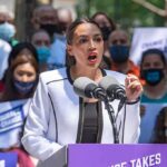 Woman speaking at outdoor rally behind microphones