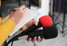 Prediction Market Faces Insider Trading Questions Journalist holding two microphones while writing in a notebook