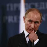 man in suit at podium touching his face