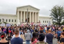 $2M Relief Fund Halted After 200+ Fraud Flags David Givens at a large protest outside a neoclassical courthouse