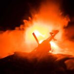 Toy helicopter silhouette against fiery explosion at night