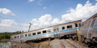 An overturned train on a railway track surrounded by vegetation