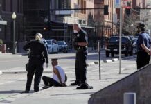 YouTuber Arrested After Reported Domestic Dispute Police officers detain a seated man on a city sidewalk