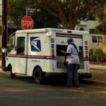 Mail carrier standing behind a USPS truck on a suburban street
