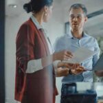 Google Veteran Launches Discovery Loop Two colleagues discussing documents in a glass-walled office