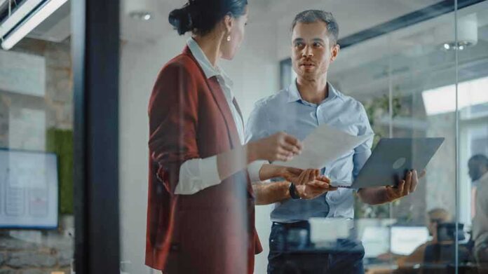 Two colleagues discussing documents in a glass-walled office