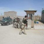 Armed soldiers patrol near a guard post outside a walled compound