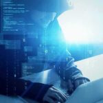 Hooded figure using a laptop with digital code overlay