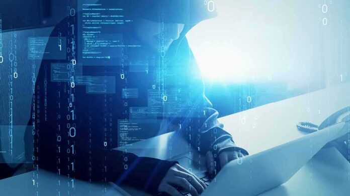 shutterstock_1984609274-1 Hooded figure using a laptop with digital code overlay