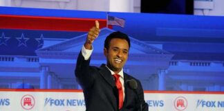 smiling man in suit at debate podium giving thumbs up