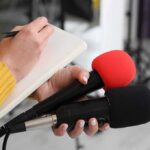 Carrier Swap Tensions: Home After 286 Days at Sea Journalist holding two microphones while writing in a notebook