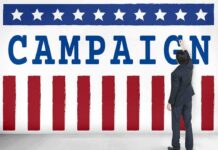 Senate Race Erupts Over Gender Care Man in suit writing on large campaign banner with stars and stripes