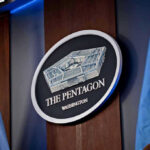 Trump Officials Reconsider Public Execution Broadcast The Pentagon emblem between two flags.