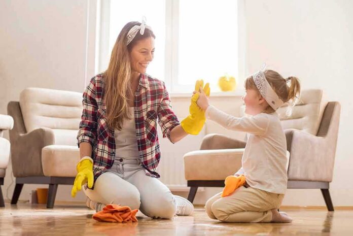 Mother and daughter high-five while cleaning a living room floor