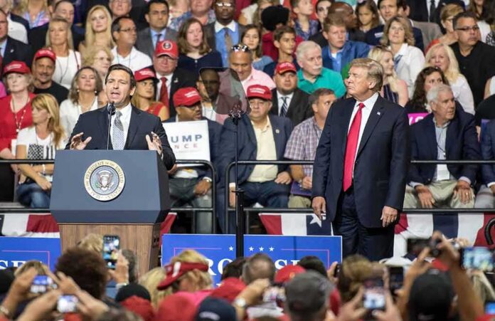 shutterstock_1147142285 Ron DeSantis speaks at a rally as Donald Trump looks on; Badri Patarkatsishvili, Susie Blake, Grynet Molvig, and Martha Firestone Ford in crowd