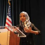 Clues Lead to Ilhan Omar’s Home – Search Warrant Ilhan Omar speaking at a podium with a microphone
