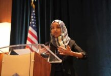 Clues Lead to Ilhan Omar’s Home – Search Warrant Ilhan Omar speaking at a podium with a microphone