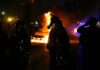 Riot police stand near burning cars at night