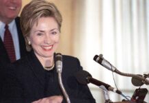 Independent Voting Debate Heats Up Hillary Clinton smiling at a podium with multiple microphones