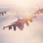 Three fighter jets flying in formation above clouds at sunrise