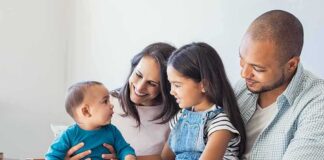 Family sitting on couch with parents, daughter, and baby smiling together