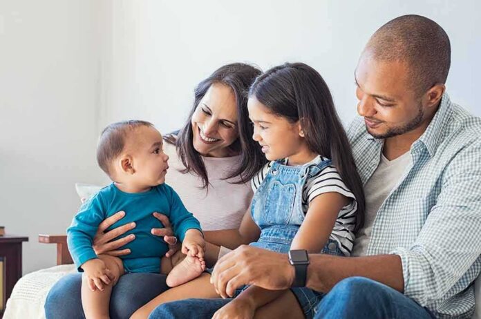 shutterstock_721479892 Family sitting on couch with parents, daughter, and baby smiling together