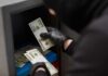 Gloved hands handling cash bundles inside a safe